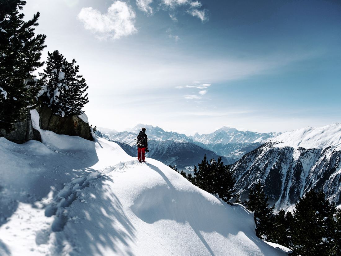 A hiker on a snowy ridge facing the Alps